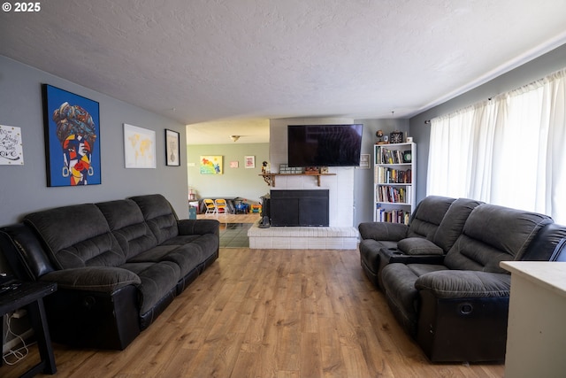 living area featuring wood finished floors, a brick fireplace, and a textured ceiling