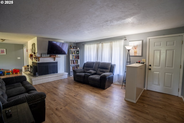 living room featuring a textured ceiling, wood-type flooring, and a brick fireplace