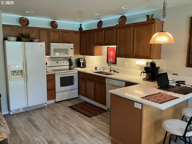 kitchen featuring white appliances, a sink, a peninsula, light countertops, and light wood finished floors