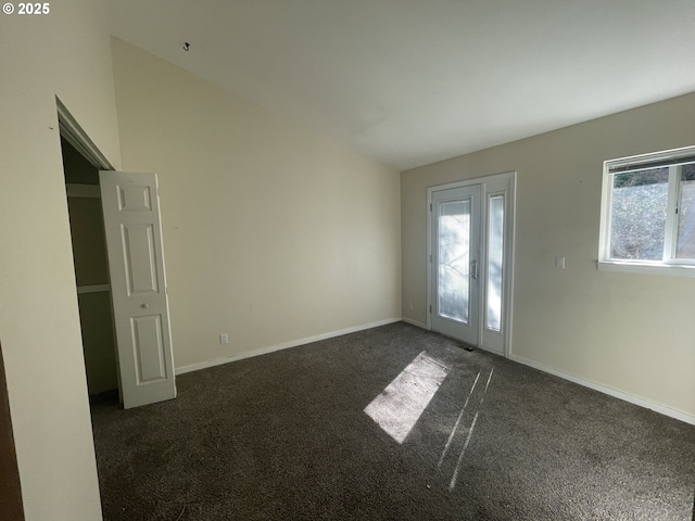 unfurnished room with lofted ceiling, dark carpet, and a healthy amount of sunlight