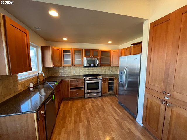 kitchen with sink, light hardwood / wood-style flooring, stainless steel appliances, and dark stone counters