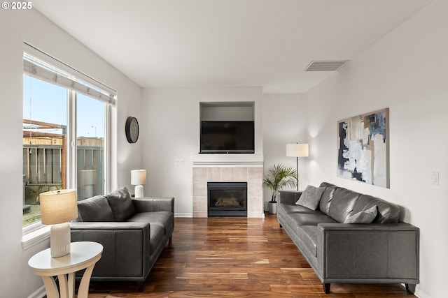 living room featuring a tiled fireplace and dark wood-type flooring