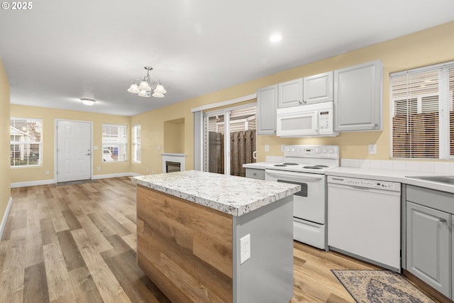 kitchen featuring a center island, a notable chandelier, light wood finished floors, light countertops, and white appliances