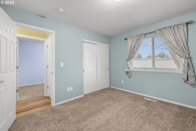 unfurnished bedroom with a textured ceiling, visible vents, a closet, and carpet flooring