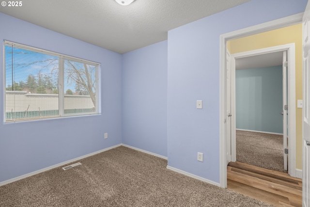 carpeted spare room with baseboards, visible vents, and a textured ceiling