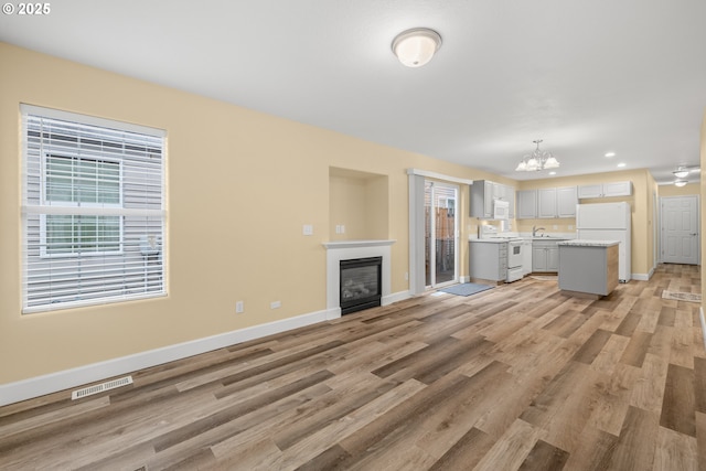 unfurnished living room with a glass covered fireplace, visible vents, light wood-style flooring, and baseboards