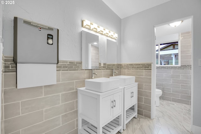 6255 SW Mad Hatter Ln, Beaverton, OR 97008 - bathroom featuring tile walls, double vanity, water heater, marble look tile flooring, and wainscoting