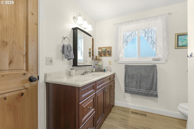 bathroom featuring vanity, toilet, baseboards, wood finished floors, and visible vents