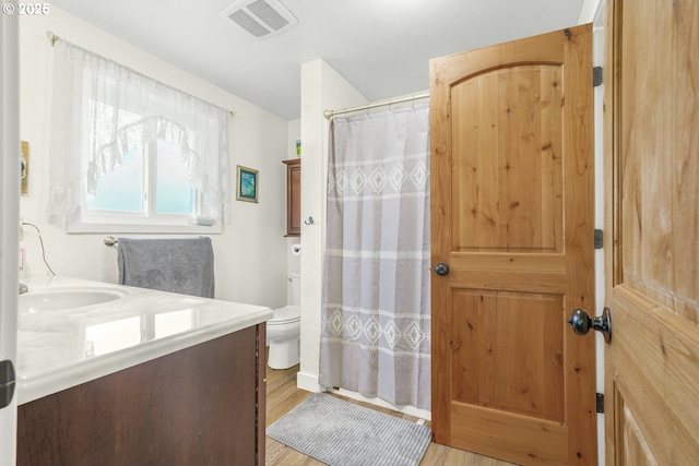 bathroom featuring vanity, toilet, curtained shower, wood finished floors, and visible vents