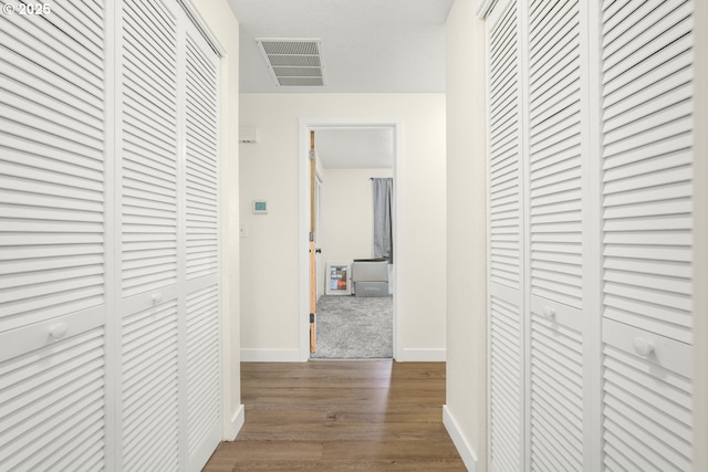 corridor with baseboards, visible vents, and dark wood finished floors