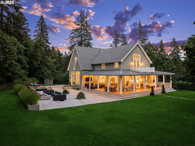 back house at dusk featuring a balcony, a lawn, and a patio area