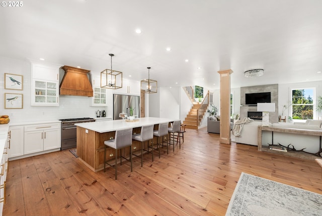 kitchen with a breakfast bar, appliances with stainless steel finishes, white cabinetry, a center island, and custom exhaust hood