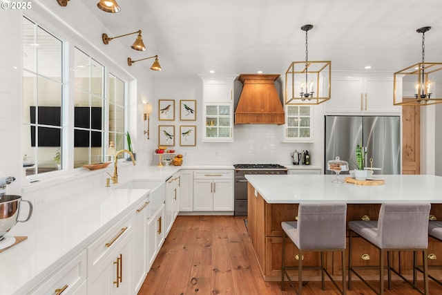 kitchen featuring sink, white cabinetry, hanging light fixtures, custom range hood, and stainless steel appliances