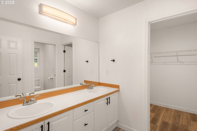 full bath with double vanity, a sink, wood finished floors, and toilet