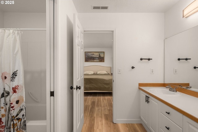 ensuite bathroom featuring ensuite bath, vanity, baseboards, wood finished floors, and visible vents