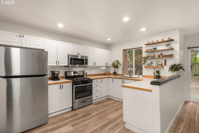 kitchen with a sink, white cabinets, light wood finished floors, a peninsula, and stainless steel appliances
