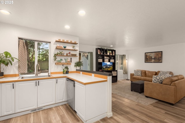 kitchen featuring a sink, a peninsula, white cabinetry, stainless steel dishwasher, and visible vents