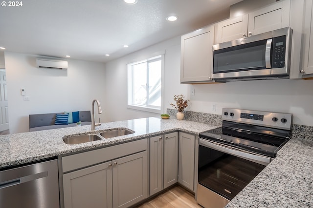 kitchen featuring appliances with stainless steel finishes, sink, light hardwood / wood-style flooring, light stone counters, and an AC wall unit