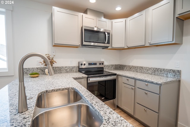 kitchen featuring appliances with stainless steel finishes, sink, light stone counters, and gray cabinetry