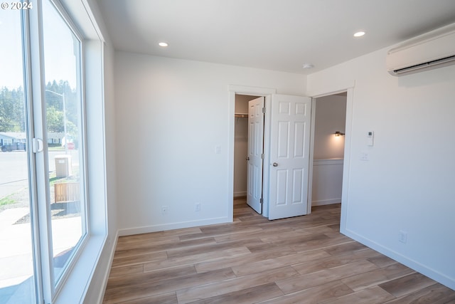 empty room featuring light wood-type flooring, a wealth of natural light, and a wall mounted air conditioner