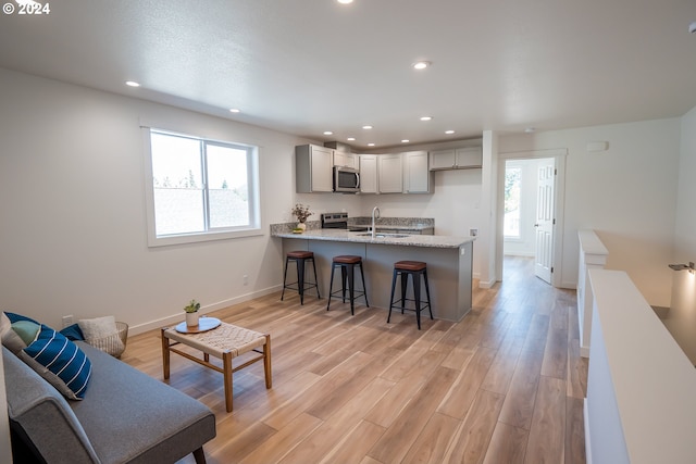 kitchen with kitchen peninsula, gray cabinetry, stainless steel appliances, and light hardwood / wood-style floors