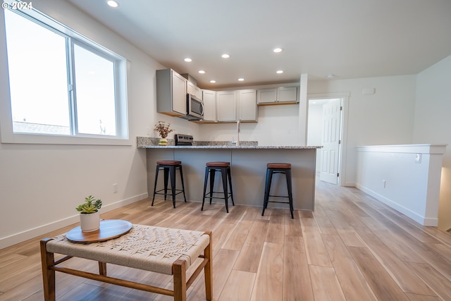 kitchen with kitchen peninsula, gray cabinets, light stone counters, and light hardwood / wood-style flooring