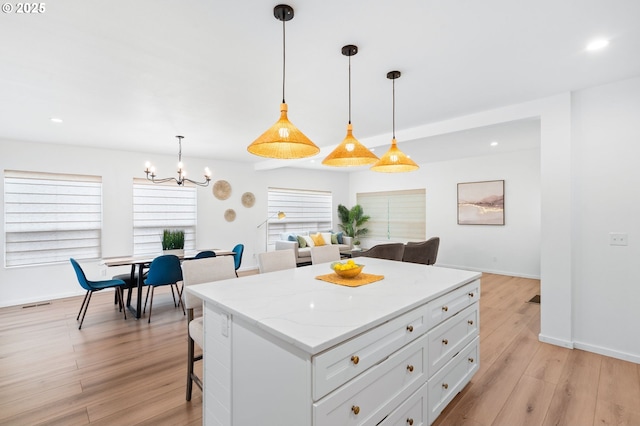 kitchen featuring white cabinetry, an inviting chandelier, a kitchen breakfast bar, light stone countertops, and pendant lighting