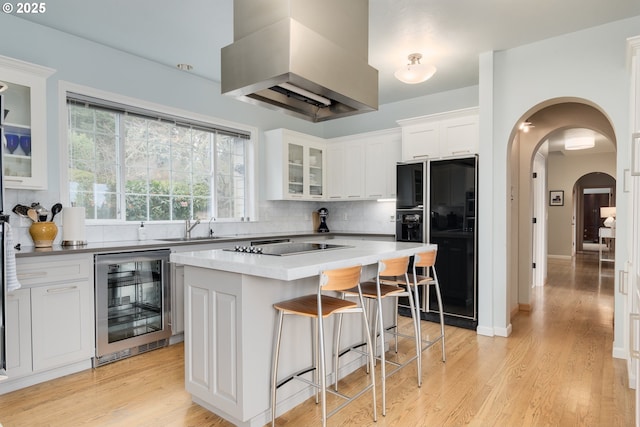 kitchen featuring a kitchen island, range hood, white cabinets, wine cooler, and black appliances