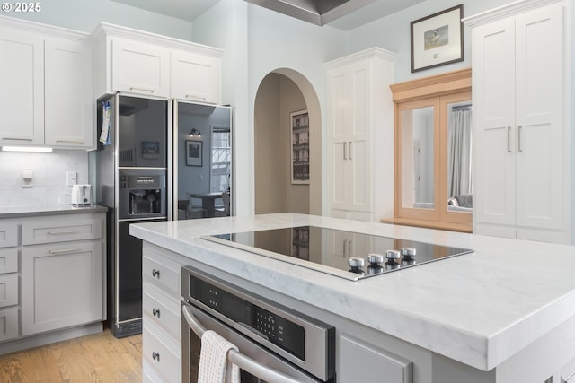 kitchen featuring backsplash, white cabinets, light wood-type flooring, and black appliances