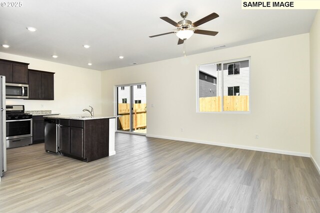 kitchen with dark brown cabinetry, ceiling fan, light hardwood / wood-style flooring, a center island with sink, and appliances with stainless steel finishes