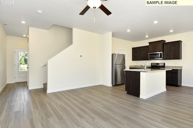 kitchen with a center island with sink, light hardwood / wood-style flooring, ceiling fan, light stone countertops, and appliances with stainless steel finishes