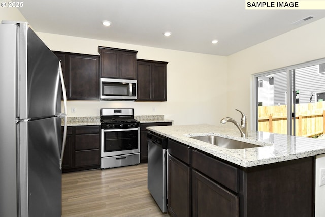 kitchen featuring dark brown cabinetry, sink, light hardwood / wood-style flooring, an island with sink, and appliances with stainless steel finishes