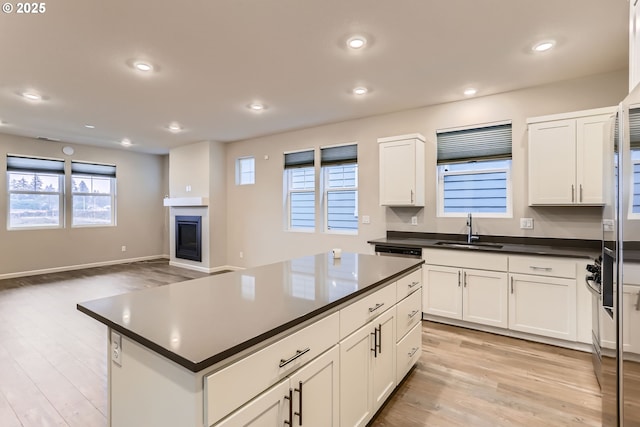 kitchen with white cabinetry, a center island, a large fireplace, and sink