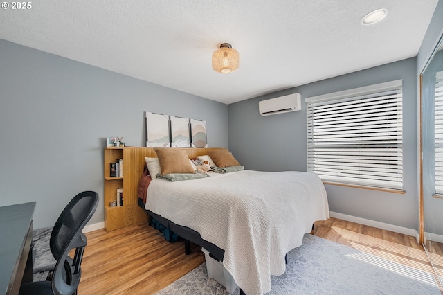 bedroom featuring baseboards, recessed lighting, a wall unit AC, and light wood finished floors