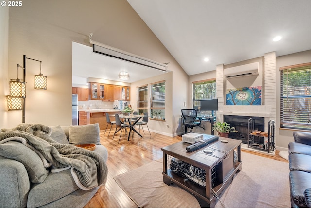 living room with baseboards, light wood-type flooring, a fireplace, a wall mounted air conditioner, and high vaulted ceiling