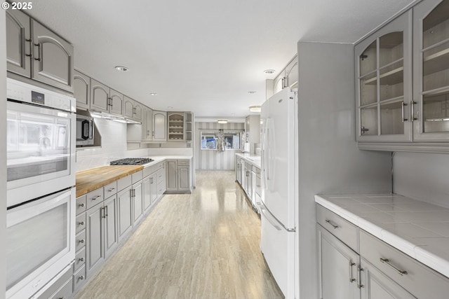 kitchen with decorative backsplash, appliances with stainless steel finishes, tile countertops, and light hardwood / wood-style flooring