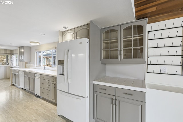 kitchen featuring sink, tile countertops, light wood-type flooring, gray cabinets, and white appliances