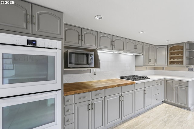 kitchen with gray cabinetry, butcher block countertops, backsplash, and appliances with stainless steel finishes