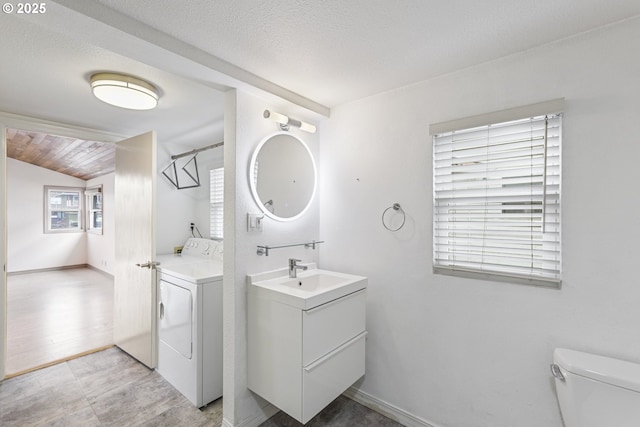 bathroom with toilet, vaulted ceiling, a textured ceiling, vanity, and washer and clothes dryer