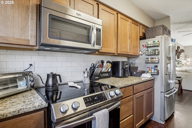 kitchen with stainless steel appliances, dark wood-style floors, a ceiling fan, brown cabinets, and glass insert cabinets