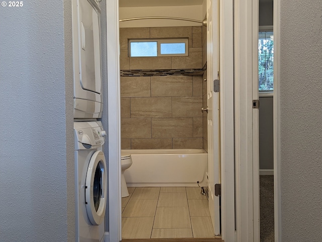 bathroom featuring tile patterned flooring, tiled shower / bath, stacked washer / drying machine, and toilet