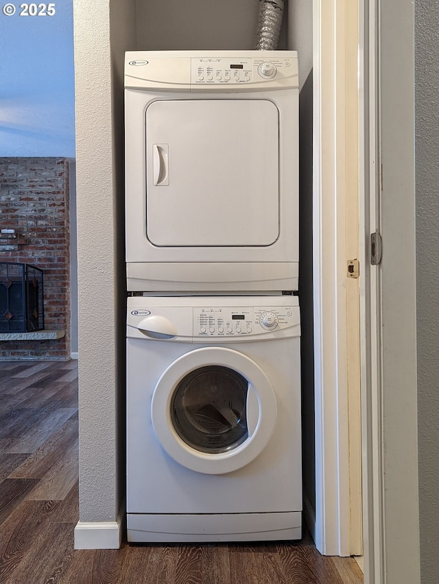 clothes washing area with stacked washer / dryer, a brick fireplace, and dark hardwood / wood-style floors