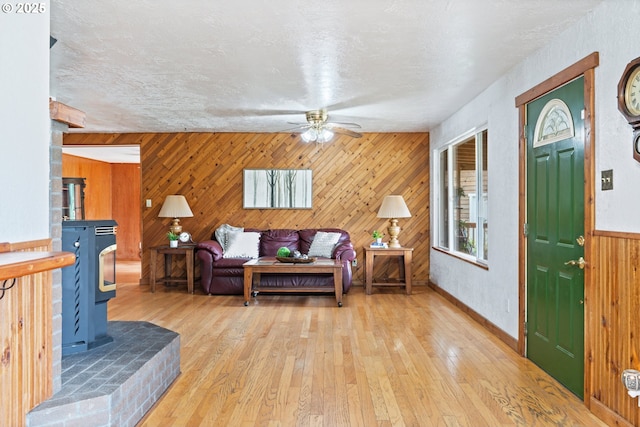 11754 Colvin Rd, Clatskanie, OR 97016 - living area with a wood stove, wood walls, a ceiling fan, light wood finished floors, and baseboards