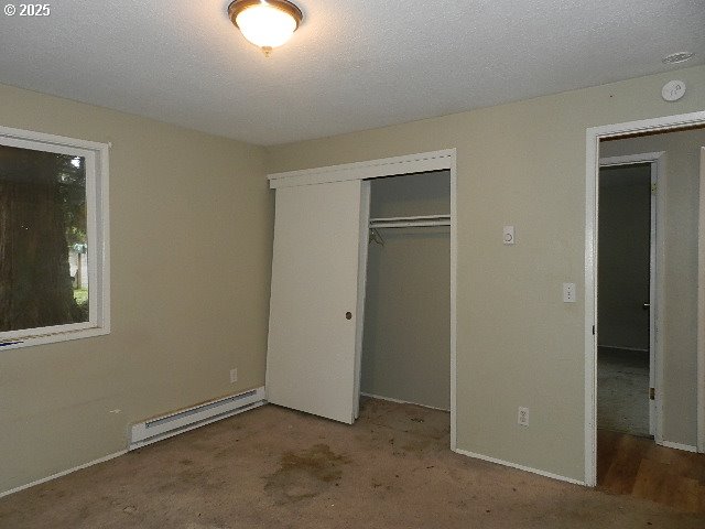 unfurnished bedroom with baseboard heating and a closet