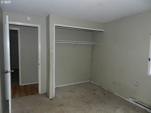 unfurnished bedroom with a closet, a textured ceiling, and a baseboard heating unit