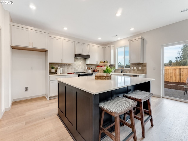 kitchen with a center island, a breakfast bar area, light countertops, light wood-type flooring, and under cabinet range hood