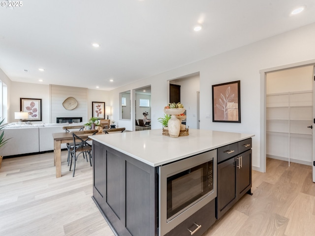 kitchen with a fireplace, light countertops, stainless steel microwave, light wood-style floors, and a kitchen island