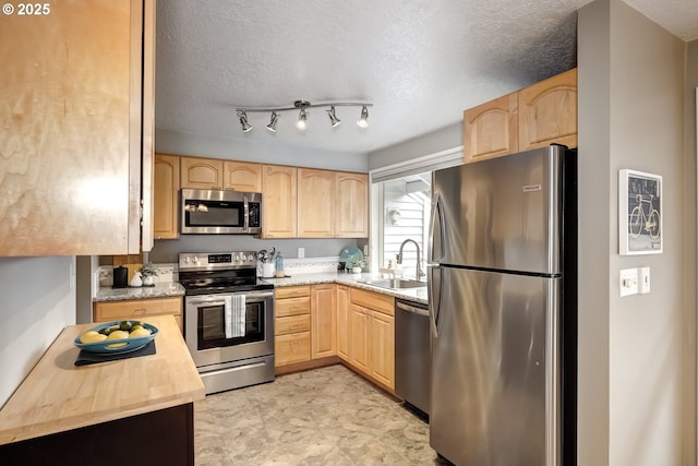 kitchen with appliances with stainless steel finishes, light brown cabinetry, sink, and a textured ceiling