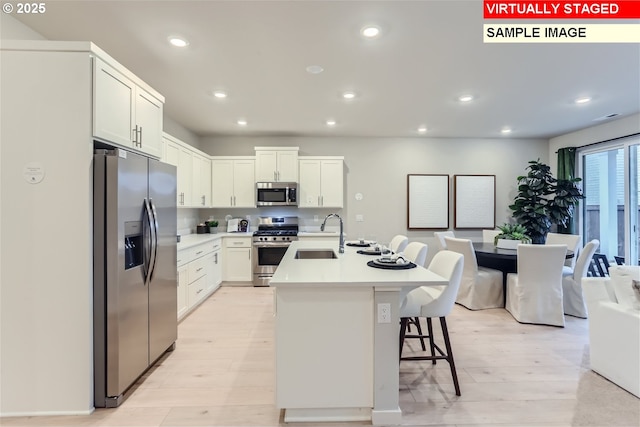 kitchen featuring a kitchen island with sink, sink, stainless steel appliances, and white cabinets