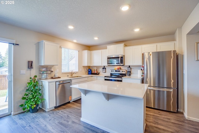 2804 N 3rd Way, Ridgefield, WA 98642 - kitchen with appliances with stainless steel finishes, a sink, a textured ceiling, a kitchen island, and wood finished floors